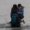 French police stand back and watch as migrant families including small children pack themselves onto small boats heading across the Channel to the UK