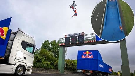 Stunt rider jumps motorcycle between two moving trucks OVER a motorway gantry - but epic backflip trick almost goes horribly wrong...