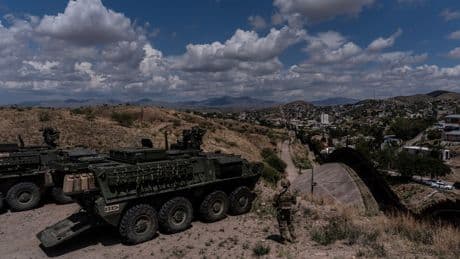 A man is halted climbing the US-Mexico border wall. Under new Trump rules, US troops sound the alarm