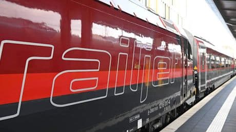 Mann springt auf fahrenden Schnellzug auf und fährt außen mit