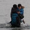 French police stand back and watch as migrant families including small children pack themselves onto small boats heading across the Channel to the UK