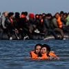 Migrants wade neck-deep into the sea off Calais carrying children on their shoulders in desperate bid to reach UK-bound boat